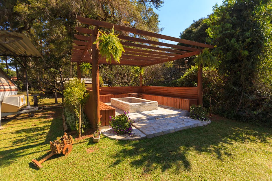 Spacious wooden gazebo in a lush garden setting with green foliage and stone flooring.